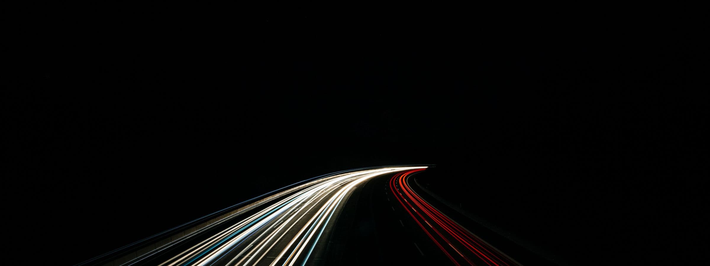 Long-exposure light trails of night traffic sweeping through the dark.