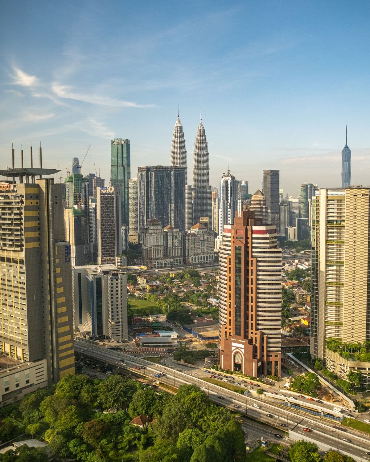 The Kuala Lumpur skyline on a clear morning, greenery in the foreground.
